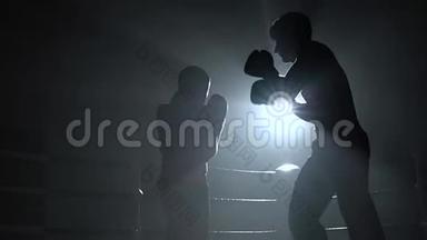 两个戴着头盔和拳击手套的人在黑暗中在擂台上战斗。 慢动作。 剪影