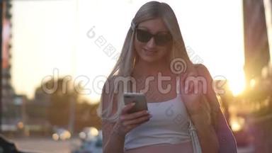 迷人的金发女郎在户外的智能手机上写信息。 一个女人，用一个数字小工具，滚动着社交