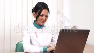 在笔记本电脑上工作的女治疗师用粉色丝带固定在她的外套上