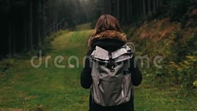 镜头跟随年轻女孩徒步旅行者走在户外的背景森林景观与高大的树木在山上。