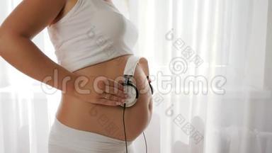 未来的年轻母亲把耳机放在大肚子上听音乐和跳舞