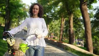 一个穿着白色T恤和蓝色牛仔裤的年轻女子，手里拿着自行车`车把，篮子里放着鲜花