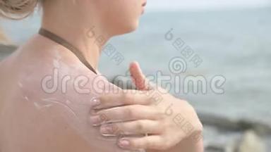 一个迷人的年轻女孩在阳光明媚的夏天坐在海滨，在她的肩膀上涂上防晒霜。 夏季