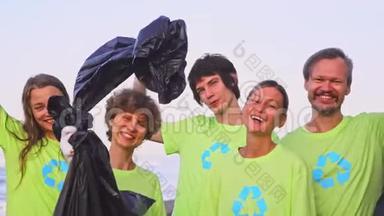 5名年轻志愿者身穿绿色t恤衫，将图像回收，在<strong>海洋</strong>海滩上收集<strong>垃圾</strong>，然后在相机上摆姿势