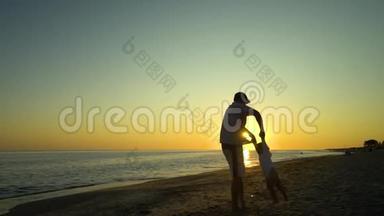 日落时，一个年轻英俊的男人和他的小女儿沿着海滨散步。 爸爸把女儿抱在怀里