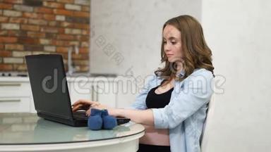 一位孕妇在论坛上写文章，妈妈拿着你的笔记本电脑坐在玻璃桌上。 白色室内客厅.. 互联网