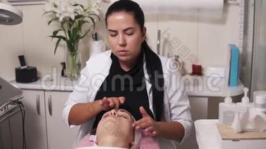 专业美容师正在水疗沙龙做面部按摩。 年轻女子在撒谎时和她的美容医生交谈