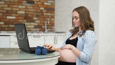 一位孕妇在论坛上写文章，妈妈拿着你的笔记本电脑坐在玻璃桌上。 白色室内客厅.. 互联网