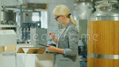 一个带着平板电脑的女人在<strong>成品</strong>仓库里做存货。 附近有几箱酒和一大箱酒