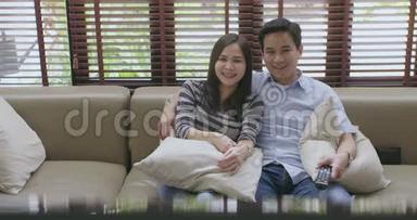 年轻的亚洲夫妇在新房子的沙发上<strong>看</strong>电视，<strong>一起看电影</strong>。