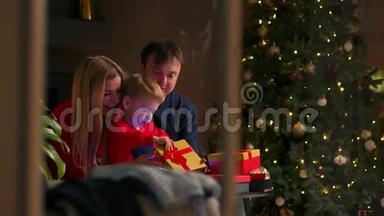 家人在圣诞节时爸爸妈妈和儿子在家里打开礼物，坐在圣诞节室内的沙发上。 温暖舒适