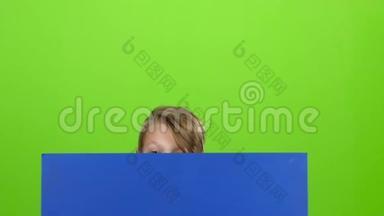 小男孩从一张蓝色的<strong>海报</strong>后面出现，看着他的<strong>表演</strong>，就像又躲起来一样。 绿色屏幕。 慢动作