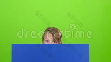 青少年从黑板后面站起来，看着它，在绿色的屏幕上表示不喜欢。 慢动作