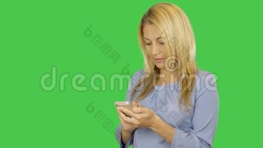 年轻女子在绿色屏幕的智能手机上键入短信。 年轻女子站着用手机。 阿尔法通道
