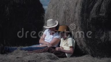 <strong>幸福</strong>的家庭母子带着平板电脑坐在田里，靠在干草卷上。 <strong>幸福</strong>家庭的概念