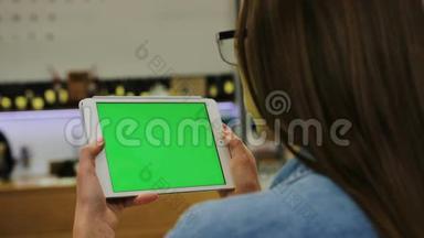 年轻有魅力的女人戴着眼镜，在咖啡馆里用<strong>绿</strong>色屏<strong>幕</strong>在平板电脑上观看<strong>视频</strong>。 特写镜头。 铬键