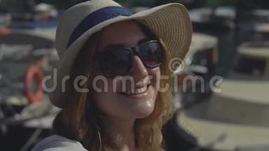 在阳光明媚的夏日，戴着帽子和太阳镜的快乐女孩的特写让自拍站在码头上。