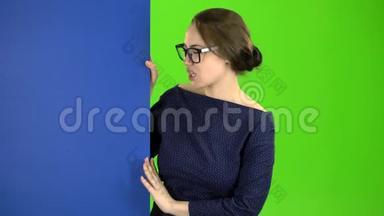 女孩从一块蓝色的木板后面窥视，并伸出大拇指。 绿色屏幕