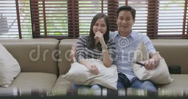 年轻的亚洲夫妇在新房子的沙发上看电视，一起看电影。