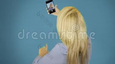 漂亮的女人在蓝色背景上用<strong>手机</strong>自拍。 微笑和<strong>旋转</strong>享受生活方式的概念。