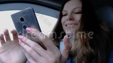 有手机的女人在车里。 年轻漂亮的黑发女人看着手机里的东西，笑了起来。
