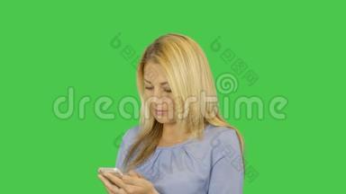 年轻的微笑，美丽的女人在智能手机上输入信息，隔离在透明的绿色屏幕背景上。 阿尔法
