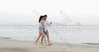 一对夫妇在海滩上用手机散步，<strong>拥抱</strong>交谈，年轻<strong>男女</strong>游客在网上交流