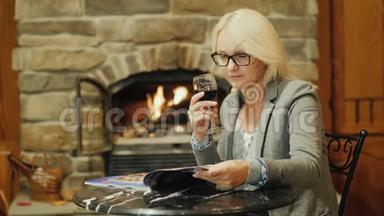 一个拿着一杯红酒的女人正在餐厅休息.. 看着桌上的杂志