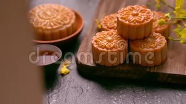 美丽的月饼在一个木盘上，茶和花在黑色背景上。 中国传统中秋节