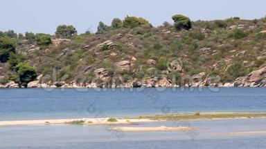 一个田园诗般的海滩和一艘快艇穿过它，海边的岩石和树木，希腊<strong>哈尔</strong>基迪基