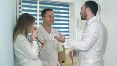男医生拿着药片在医院大厅里和另外两名医生交谈