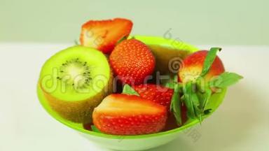 鲜奇异果和切片草莓在蓝色背景上的绿色盘子旋转成一个圆圈。 从上面看