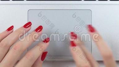 4K镜头。 女人的手`红色指甲使用和点击便携式电脑轨迹板。 俯视图，特写