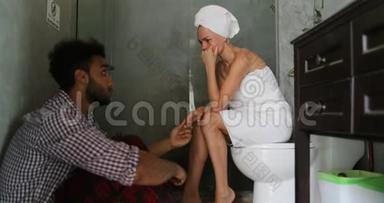 年轻夫妇在浴室里不开心，男人和女人争论有问题，女孩哭着<strong>坐在地板上</strong>的马桶<strong>上</strong>