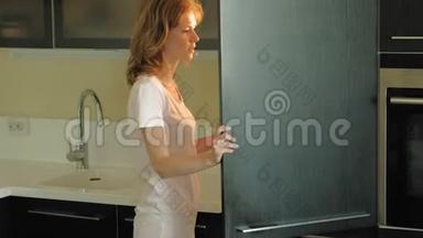 一个年轻的女人打开冰箱，选择产品。 上午