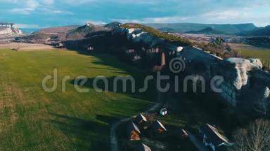 山顶的<strong>山崖</strong>和几个小房子在一片绿色的田野上，蓝天多云。 美丽的夏天