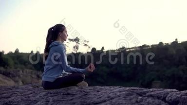 瑜伽女人坐坐冥想姿势在山崖日出