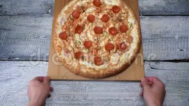 白色桌子背景上木制托盘上的美味披萨。 框架。 男人在木制托盘上用意大利辣香肠移动刚出炉的披萨