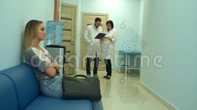 两位医生讨论诊断时，忧心忡忡的女病人在医院大厅等候