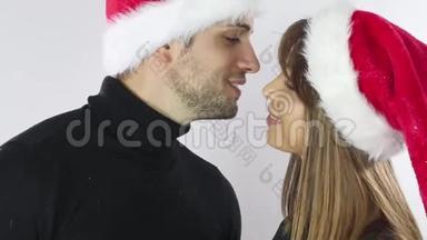 圣诞<strong>佳节</strong>快乐的一对夫妇戴着红色新年圣诞帽，男人和女人都爱笑看镜头接吻