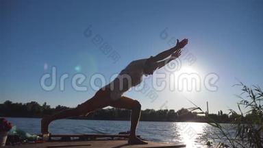 站在<strong>瑜伽馆</strong>前的运动男子剪影在湖边的一个木制码头上摆姿势。 在大自然训练的年轻人。 运动员