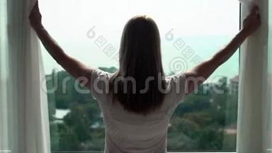 穿白色t恤的女人揭开窗帘，看着窗外。 欣赏100英尺的海景