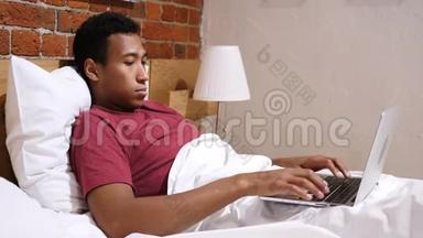 令人沮丧的非洲男人在床上工作，在笔记本电脑上工作，并<strong>应对</strong>损失