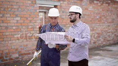 一个戴着头盔的工程师和一个长着胡须的成年<strong>建筑</strong>师考虑一个<strong>施工</strong>图，其<strong>中</strong>的方案为