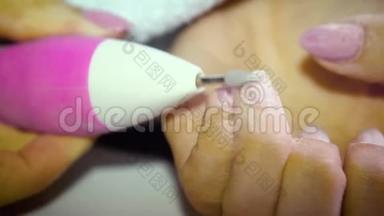 一个指甲丑陋的女孩用一台特殊的机器从指甲中去除指甲油，为修指甲做准备。 关闭