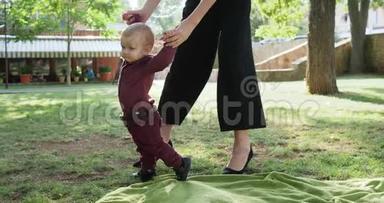 妈妈帮助儿子在户外迈出第一步，妈妈支持她的小宝宝练习他的第一步