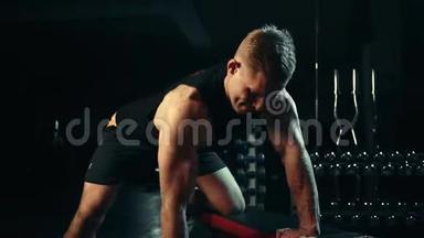 一个肌肉发达的人在黑暗的健身房里对背部肌肉做哑铃练习，举重