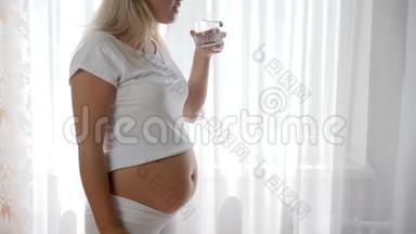 大肚腩的孕妇在白色背景下缓慢地喝清水