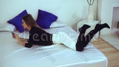 穿着黑色靴子的美丽苗条的女士躺在白色的床上
