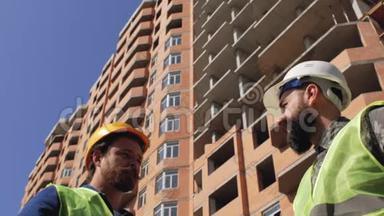 两名戴着胡须和胡子的头盔的施工管理人员在施工现场讨论施工细节。 4k